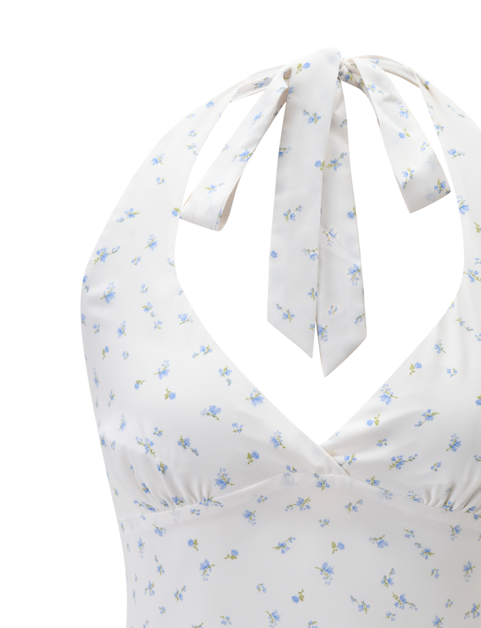 Close-up of the CALI TOP - DITSY FLORAL by TIGERMIST, a white halter neck top with blue ditsy floral print, deep V-neckline, ruched bust detail, and bow tie at the neck.