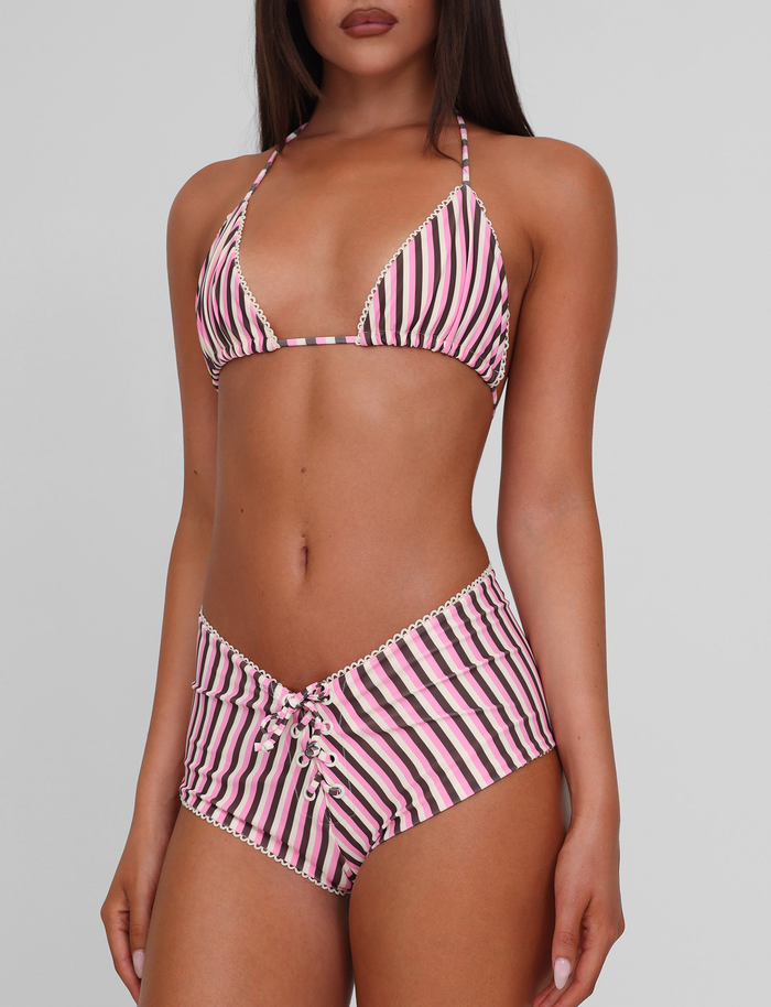 A woman models the TIGERMIST DAZZLE BIKINI TOP - STRIPE, a pink, white, and black high-stretch triangle bikini with lace-up, high-waisted bottoms, against a plain light gray background.