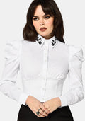 Woman wearing a white blouse with black floral details on a plain background