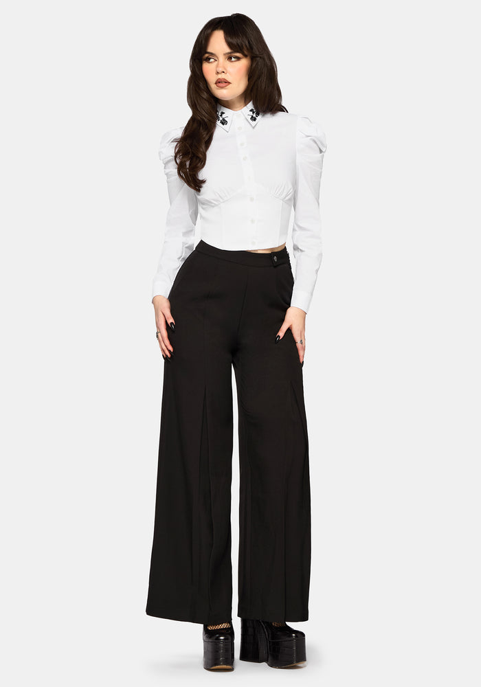 Woman wearing a white blouse and black wide leg trousers on a white background