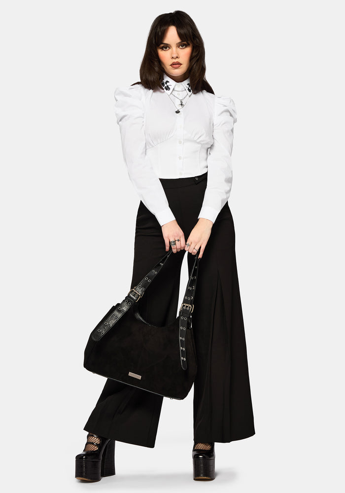Woman wearing a white blouse and black wide leg trousers holding a black handbag on a white background