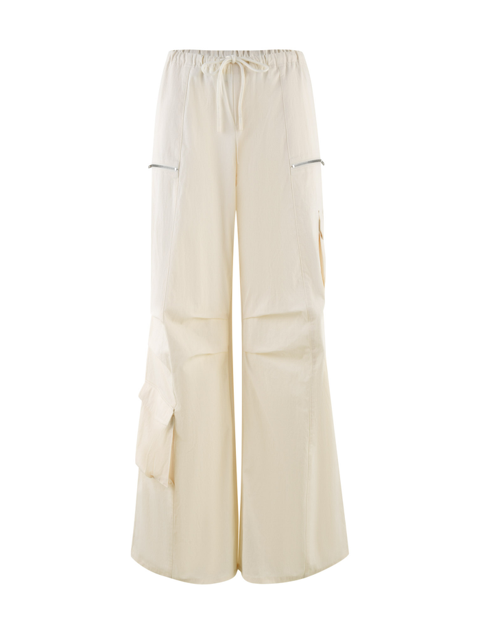 The TIGERMIST HERMIONE PANT in Soft Butter features a wide-leg cargo style with an elastic drawstring waist, zippered side pockets, and a large flap pocket, offering a loose fit for comfort and style.