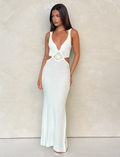 A woman with long, straight hair in a neutral pose wears the TIGERMIST JONAH MAXI DRESS in cream, featuring a sleeveless bodycon fit, deep V neckline, cut-out sides, and flared hem against a light textured wall.