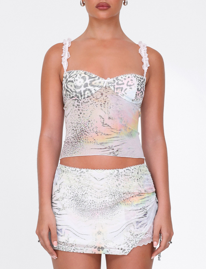 A woman wears the TIGERMIST JOSEPHINE MINI SKIRT in white animal print with ruched sides, paired with a matching lace-trim camisole. The background is plain white.