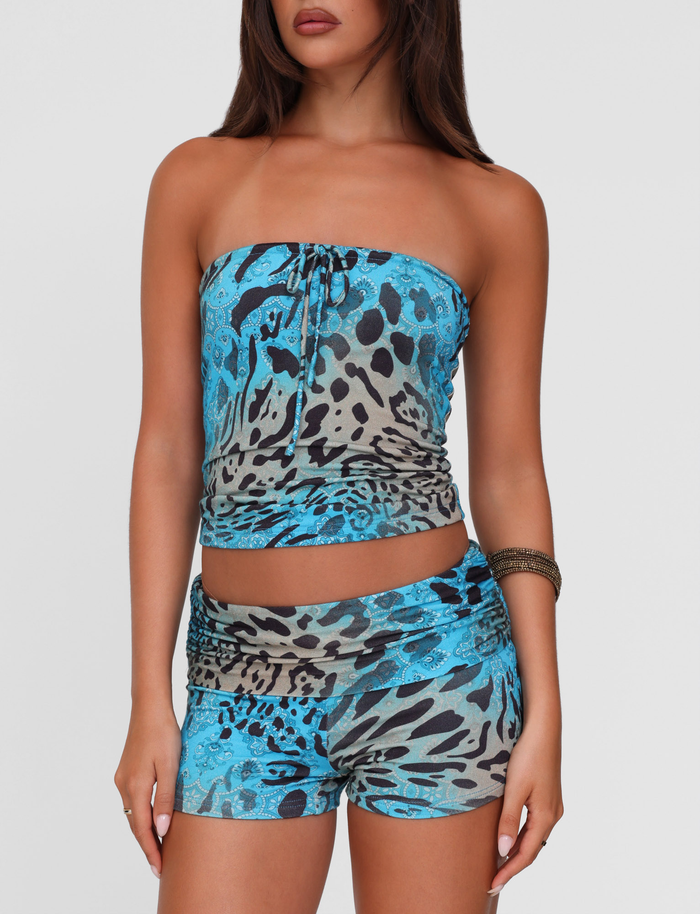 A woman models the TIGERMIST KARINA SHORT - MULTI : LEOPARD : LEOPARD SWIRL with a matching blue and gray strapless top. She has long brown hair, wears a bracelet on her right wrist, and poses against a white background with her face partially out of frame.