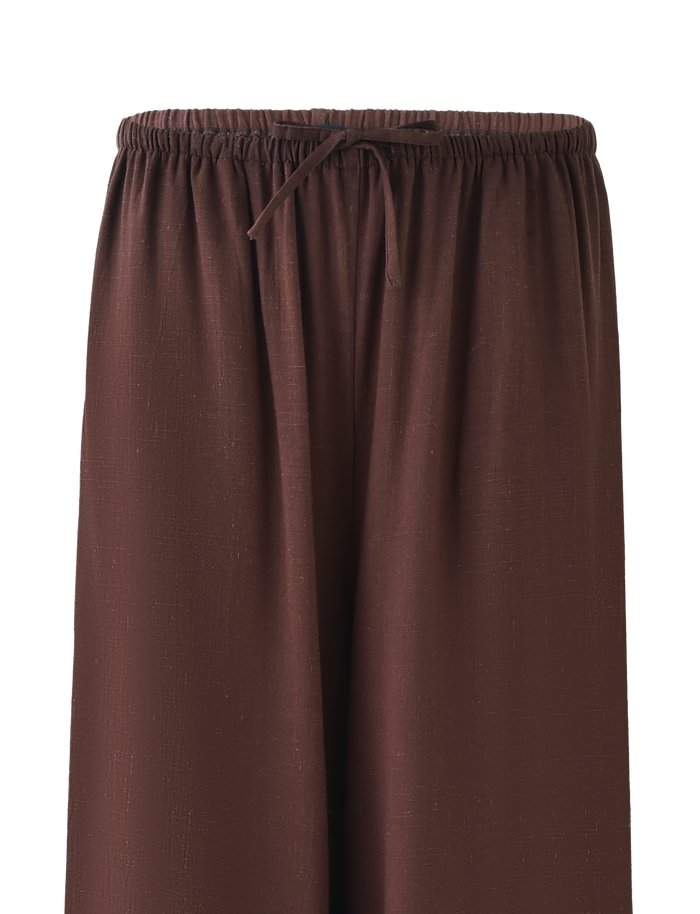 The LAINEY PANT - CHOCOLATE by TIGERMIST features wide-leg, textured brown linen, a mid-rise elastic waist with drawstring, and functional side seam pockets. Pants shown from waist down, no visible background.