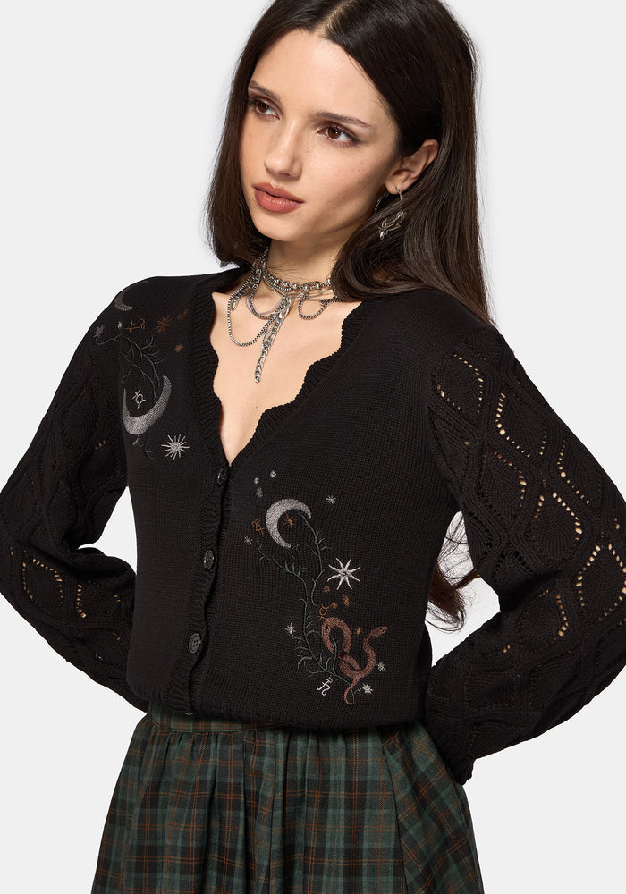 Woman wearing a black embroidered cardigan with celestial designs on a white background