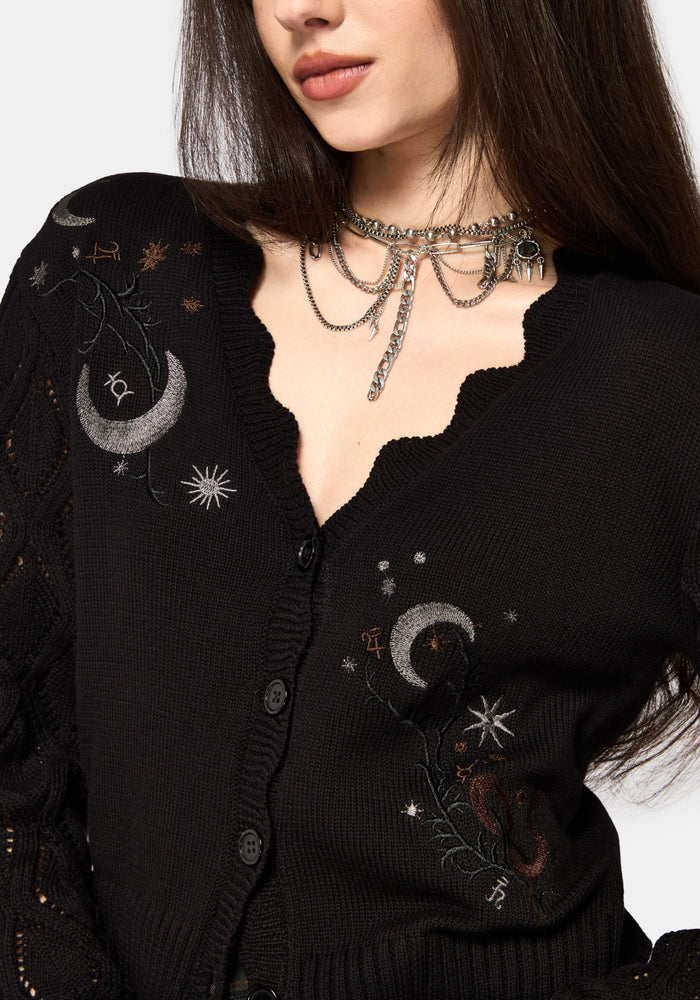 Woman wearing a black embroidered cardigan with celestial designs on a white background