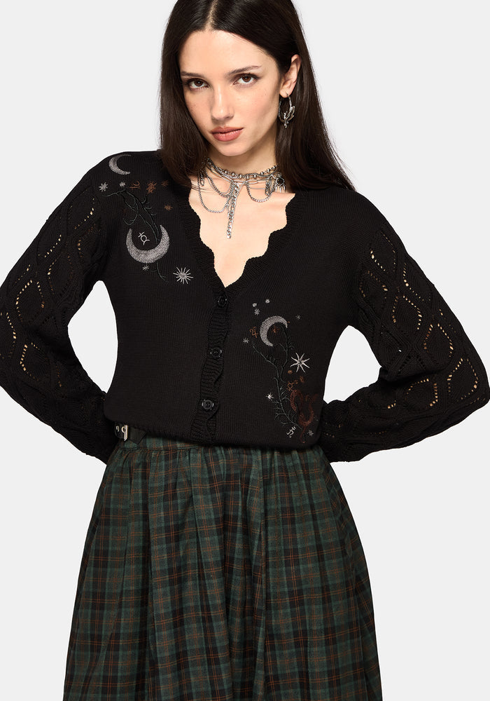 Woman wearing a black cardigan with celestial designs and a plaid skirt on a white background