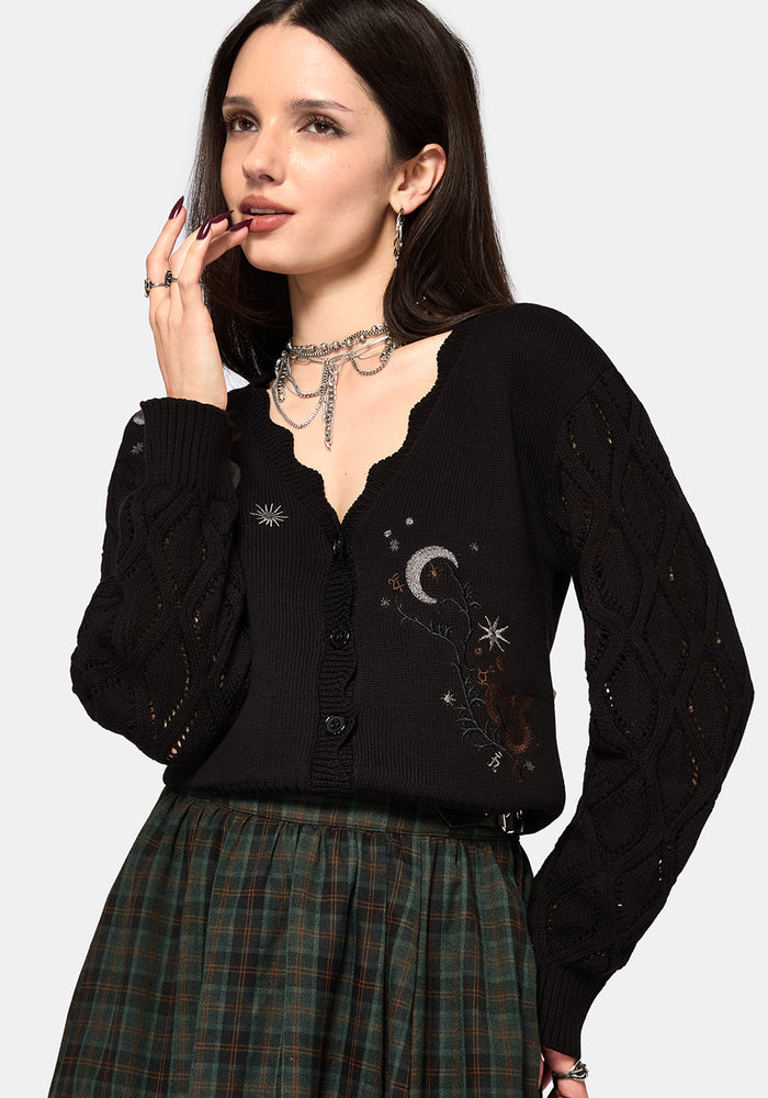 Woman wearing a black cardigan with celestial designs on a white background