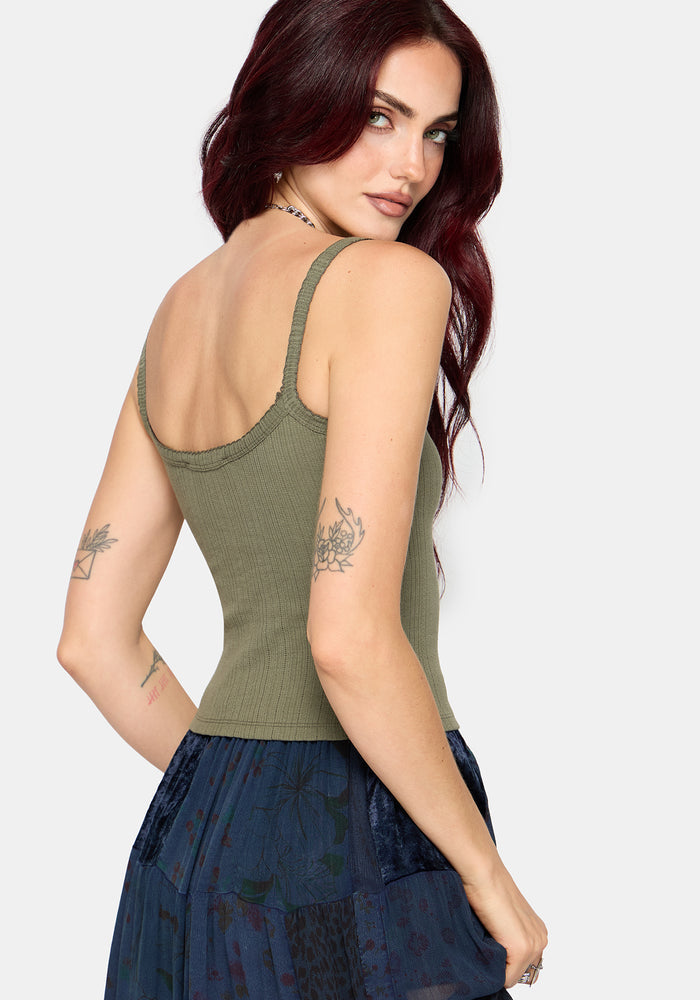Woman wearing a khaki sleeveless vest with thin straps, cropped length and blue butterfly embroidery in center against a white studio background