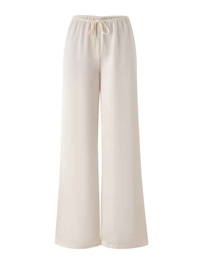 The MAURA PANT by TIGERMIST, shown in white, features wide legs and is crafted from drapey satin fabric with an elastic waistband and adjustable drawstring waist, displayed on a white background.