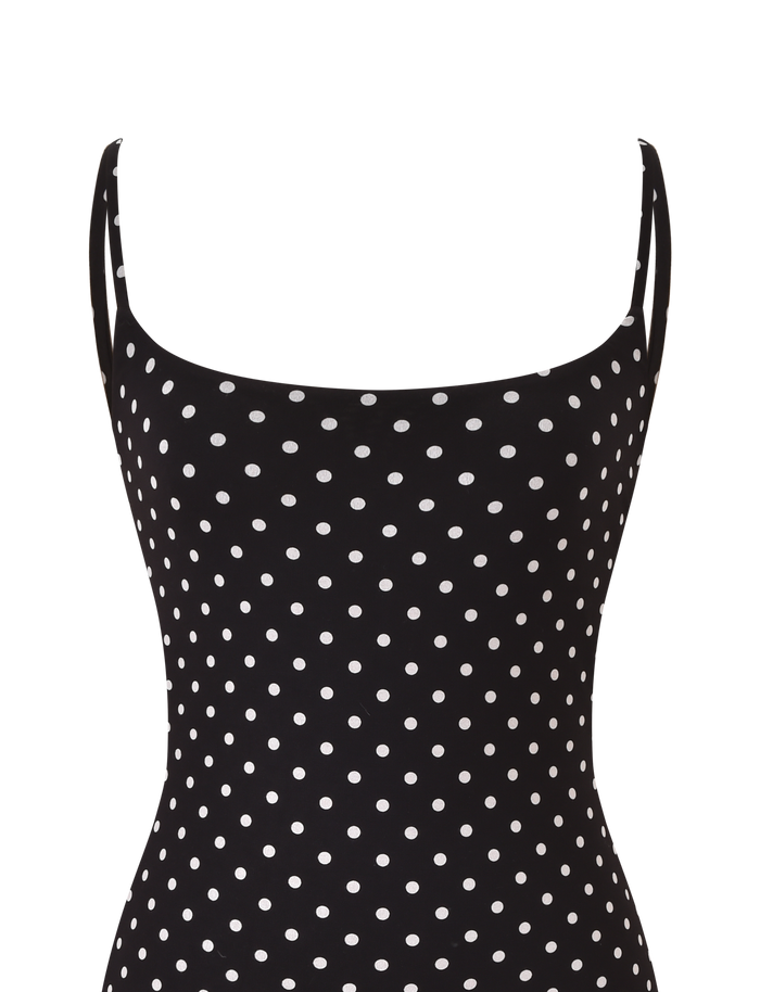 A close-up of the TIGERMIST MINERVA MINI DRESS 2.0 in black polka dot, featuring adjustable shoulder straps, white spots, and a straight neckline.
