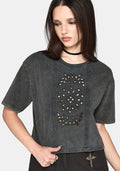 A woman wearing a dark gray washed short-sleeve crop top with a vertical panel of stud cut outs and embroidery, paired with black pants and a black choker against a light gray background.