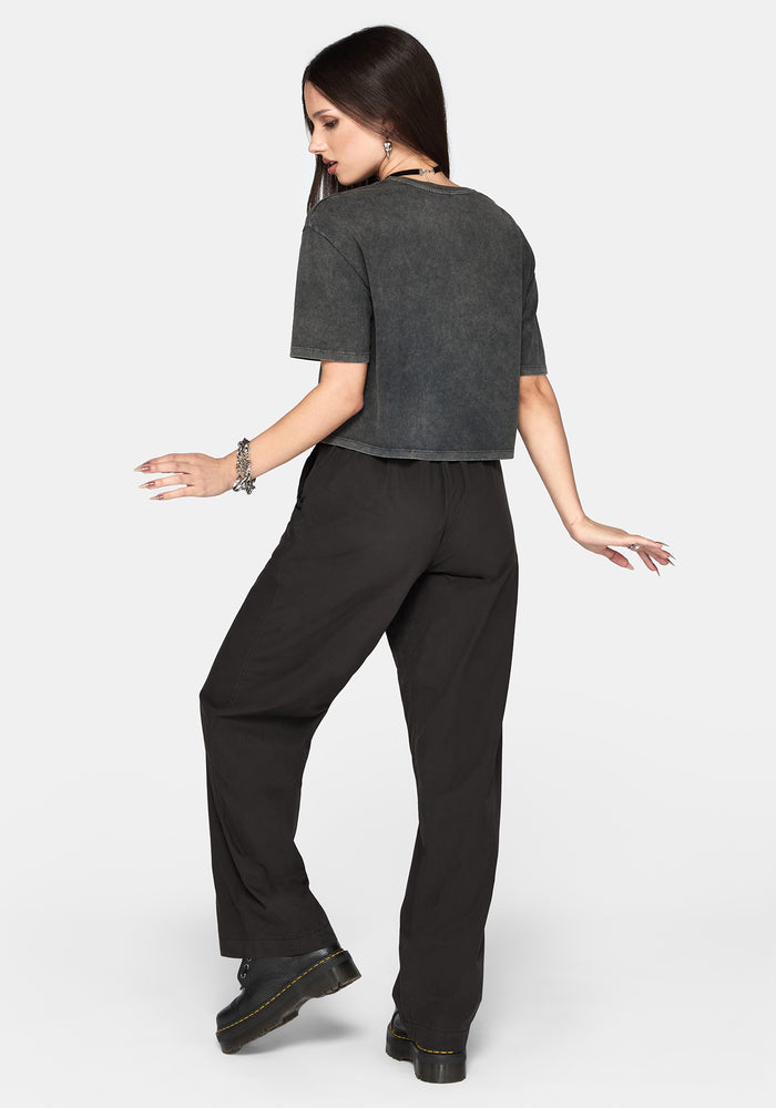 A woman posing from the back wearing a dark gray cropped t-shirt and black wide-leg trousers against a light gray background.