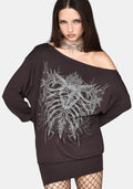 A woman modeling an oversized off-the-shoulder black sweatshirt dress with a large white skeleton rib cage graphic on the front, paired with fishnet tights and a silver choker against a light gray background.