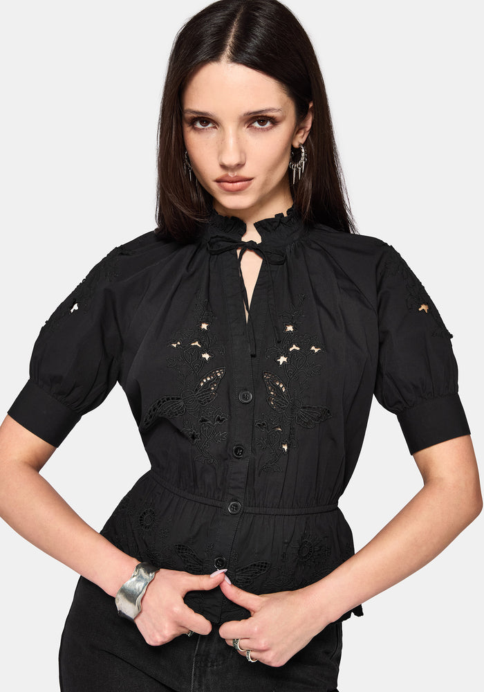 Woman wearing a black blouse with floral cut out details on a white background