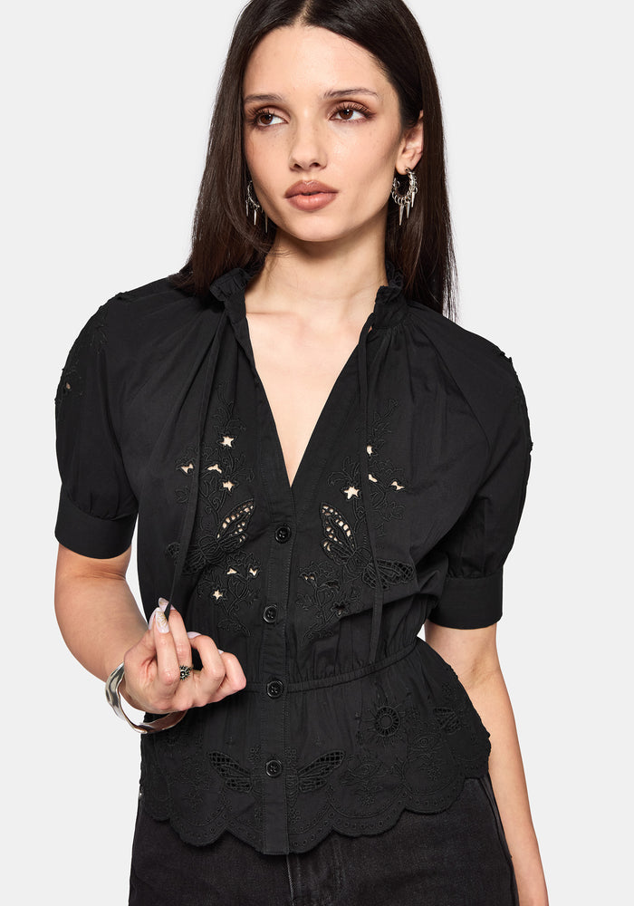 Woman wearing a black blouse with floral cut out details on a white background