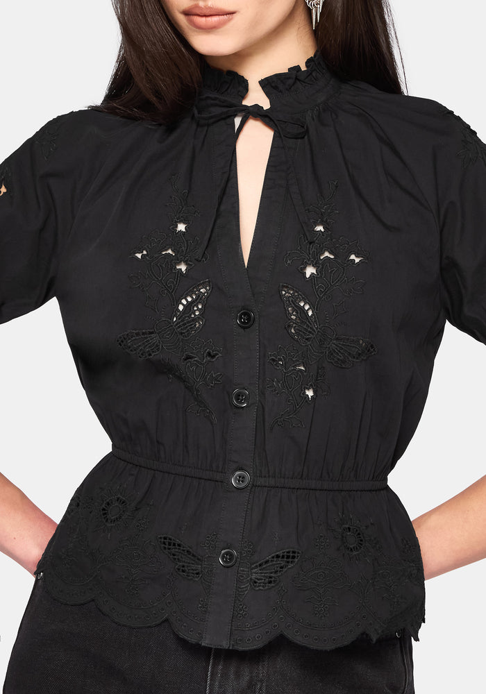 Woman wearing a black blouse with floral cut out details on a white background