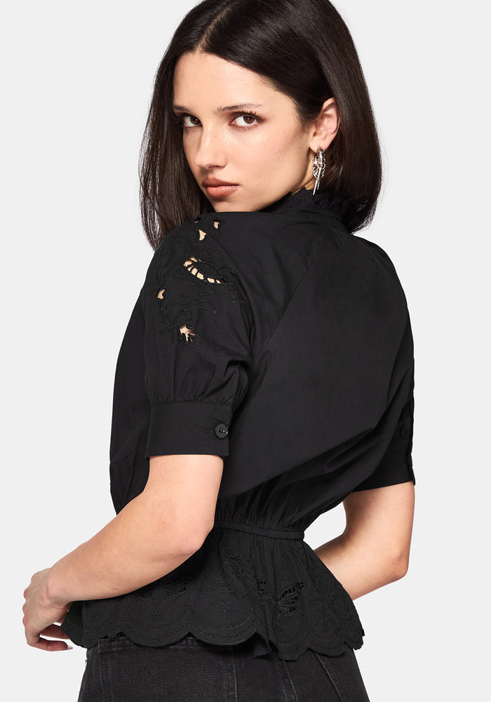 Woman wearing a black blouse with ruffled details on a white background