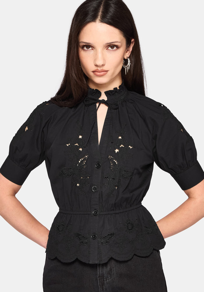 Woman wearing a black blouse with intricate designs on a plain background